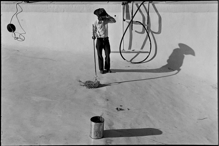 Worker in cowboy hat cleaning empty pool