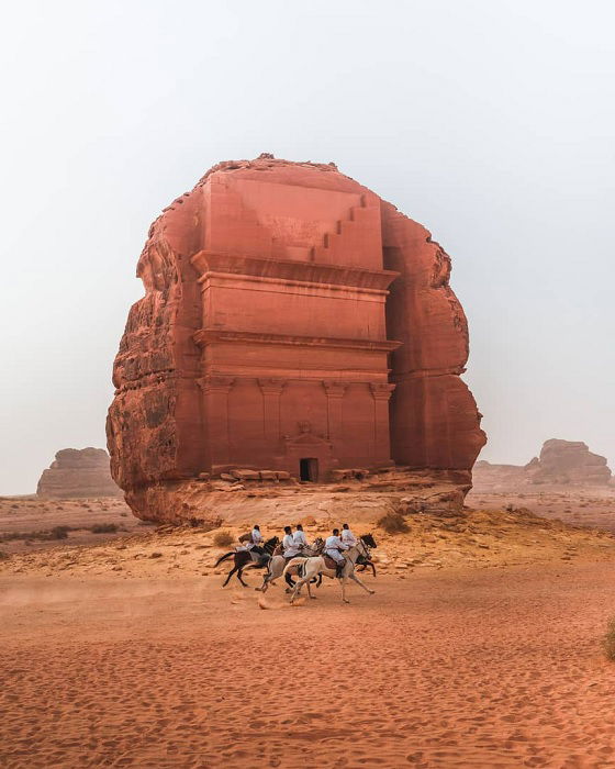 Horse riders passing large rock monument