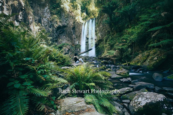 Woman sitting at foot of waterfall