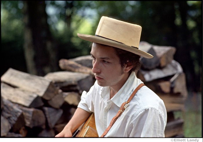 Bob Dylan in hat playing guitar outside