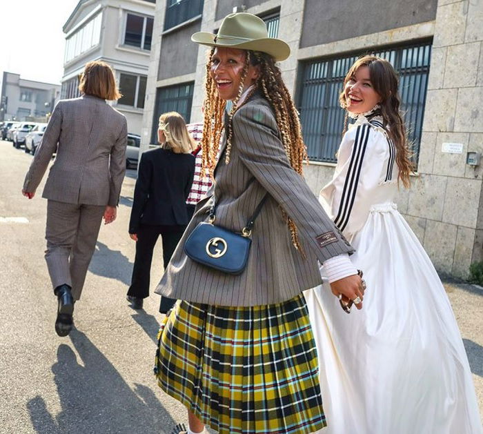 Two young women walking holding hands looking back over their shoulders