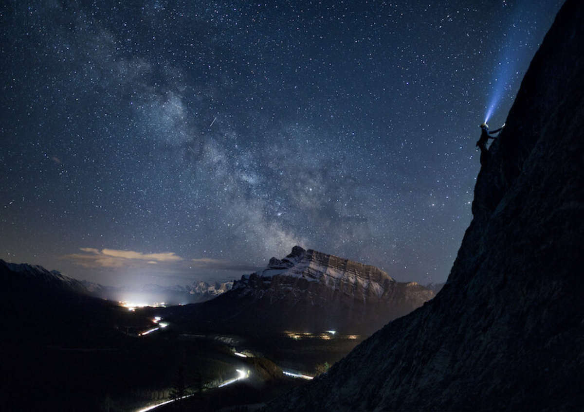 photograph of mountain range at night with climber with head torch 