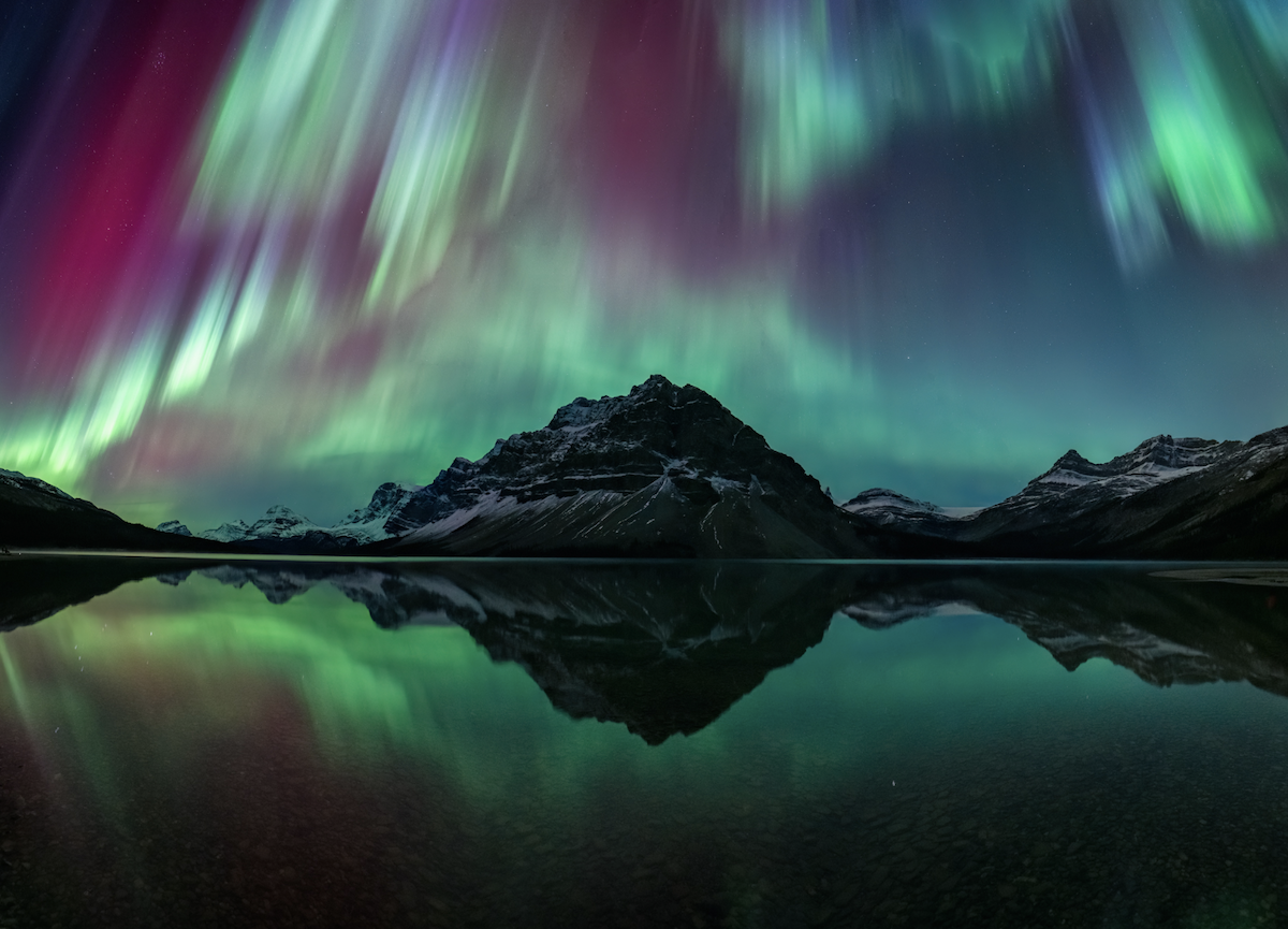 photograph of mountain with lake in foreground and northern lights in background