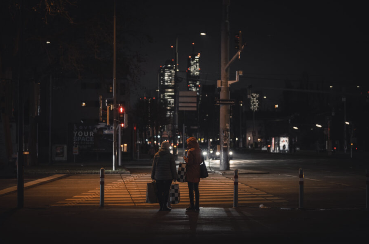 two people standing at a crossing at night 